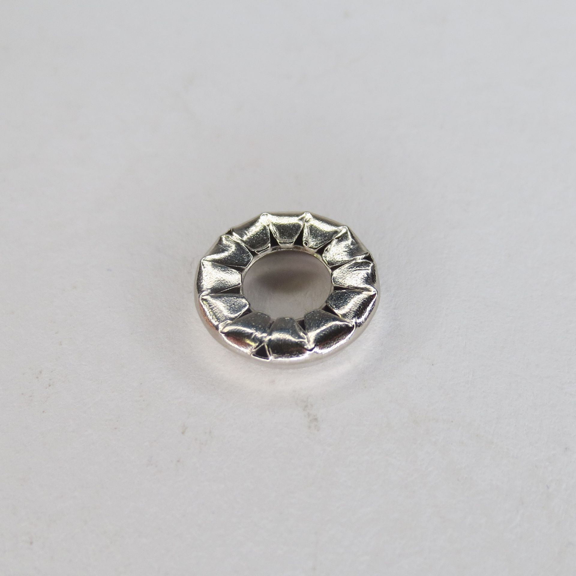 Auf einer weißen Fläche befindet sich ein silberner Ring mit einem Loch in der Mitte.