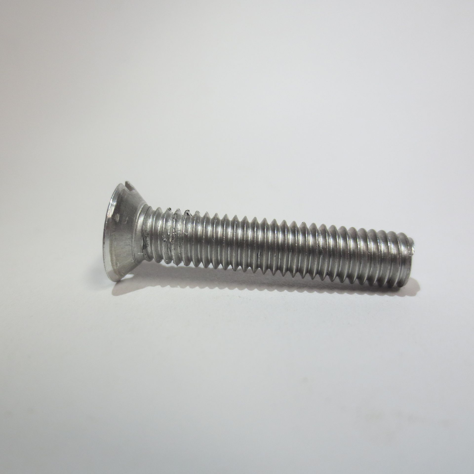 Eine Edelstahlschraube liegt auf einer weißen Fläche..