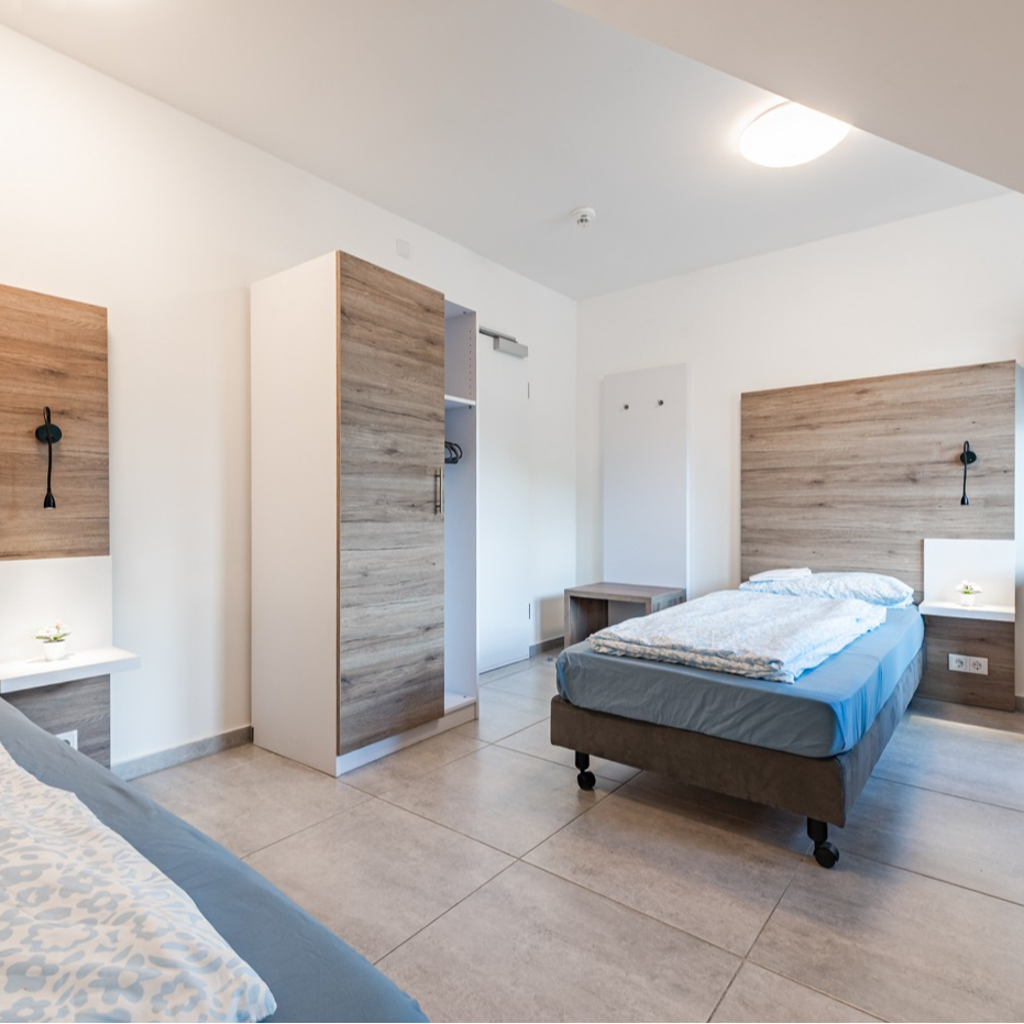 Bedroom with two single beds, light wood headboards and closet, tiled floor, white walls.