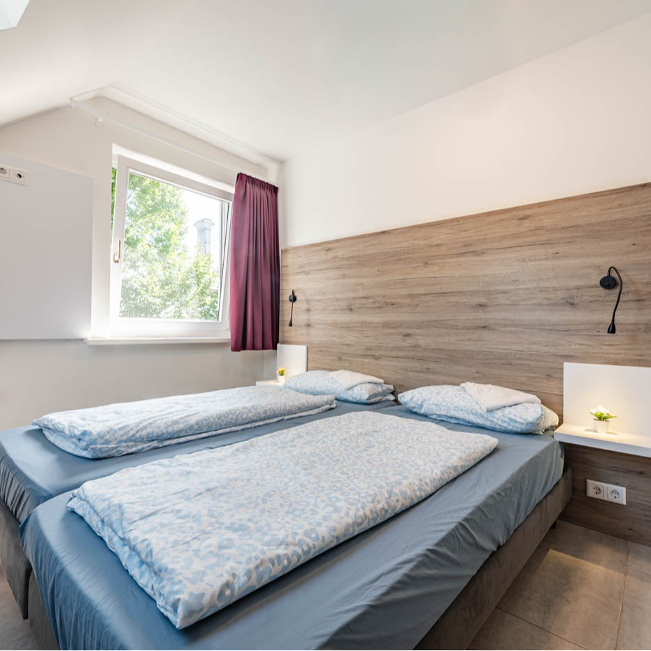 Bedroom with two single beds, window, wood headboard, and bedside lamps.