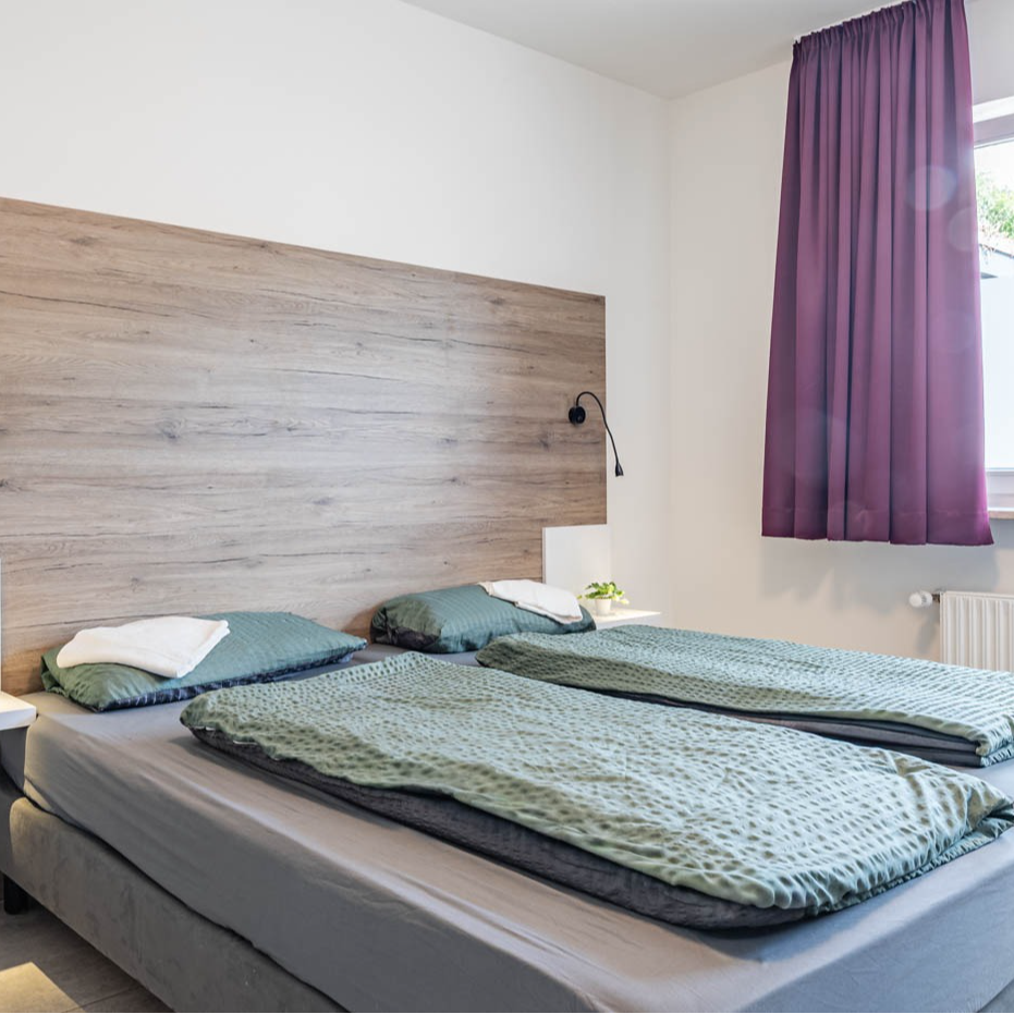 Bedroom with two beds, gray bedding, wooden headboard, purple curtain.