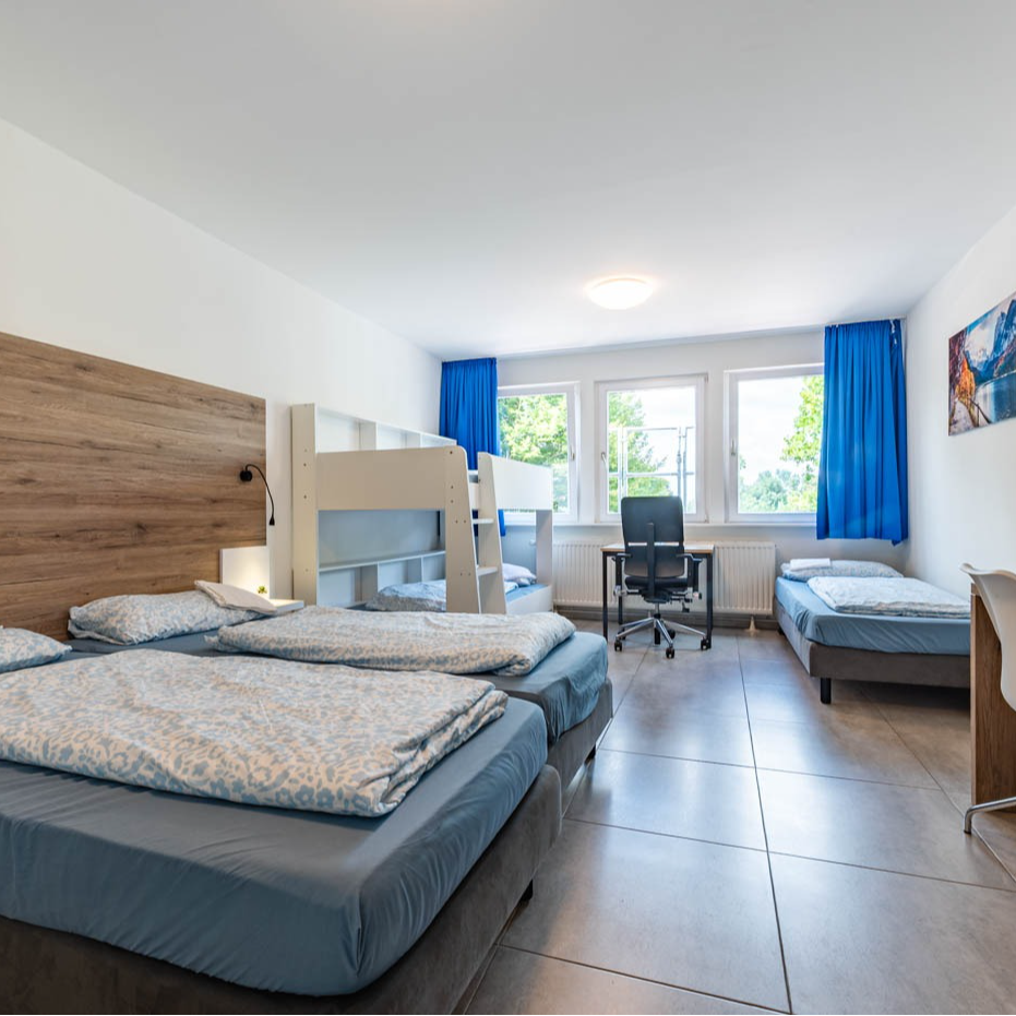 Bedroom with a bunk bed, two twin beds, desk, and large window with blue curtains.