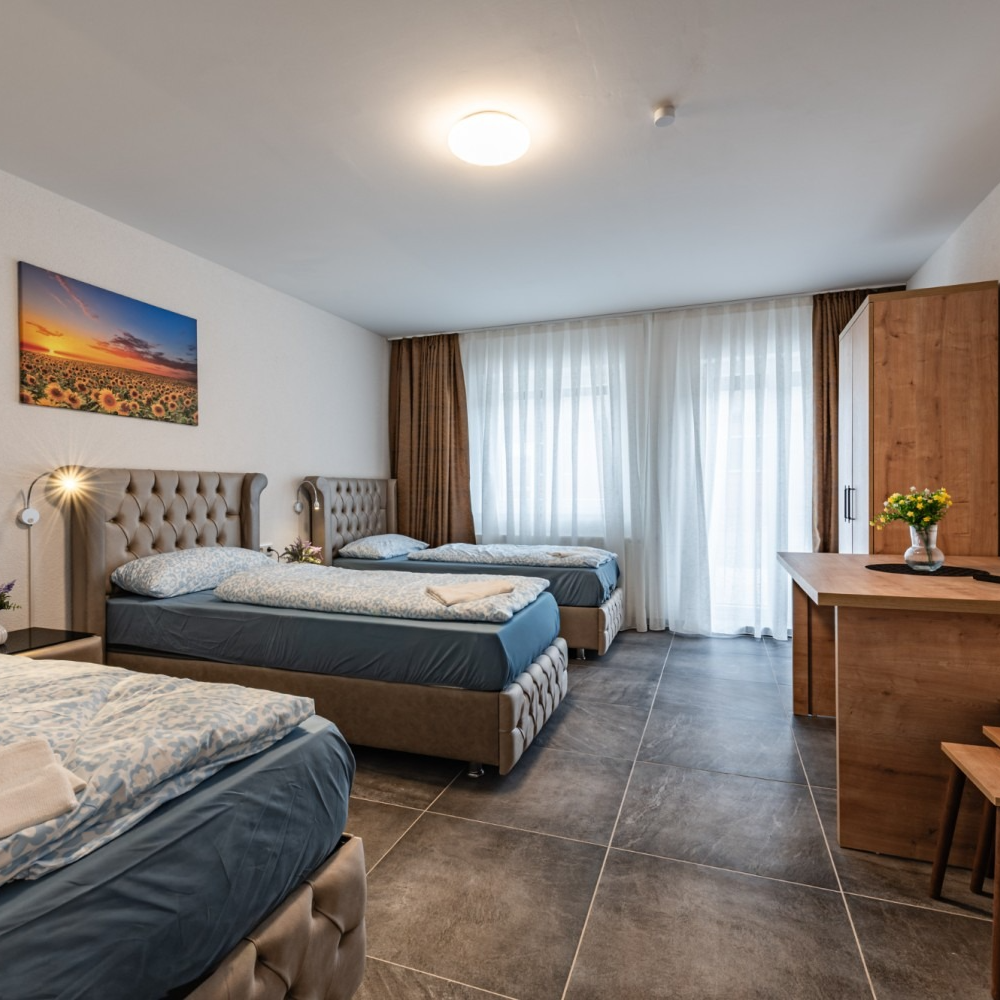 Three beds in a room, with window, desk, and sunflower painting.
