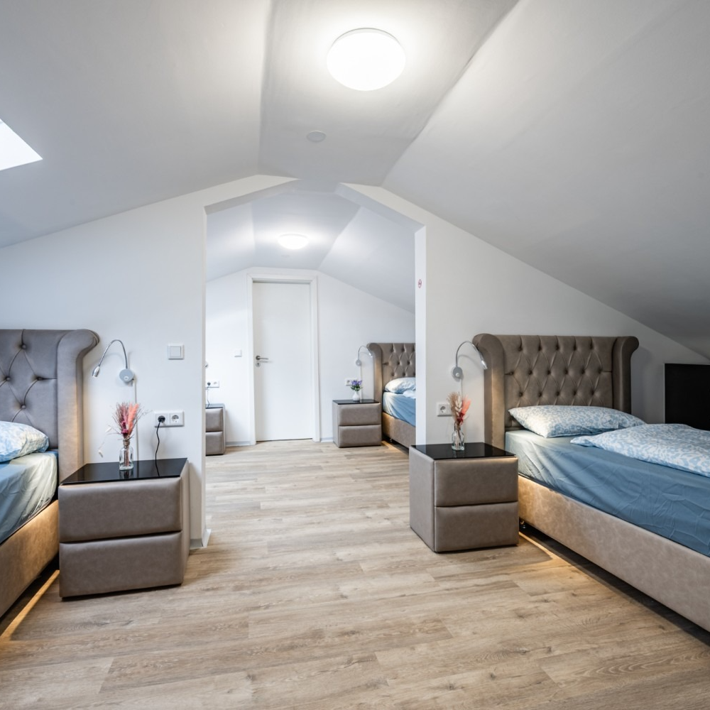 Bedroom with three twin beds, neutral tones, under slanted ceiling, and light wood flooring.