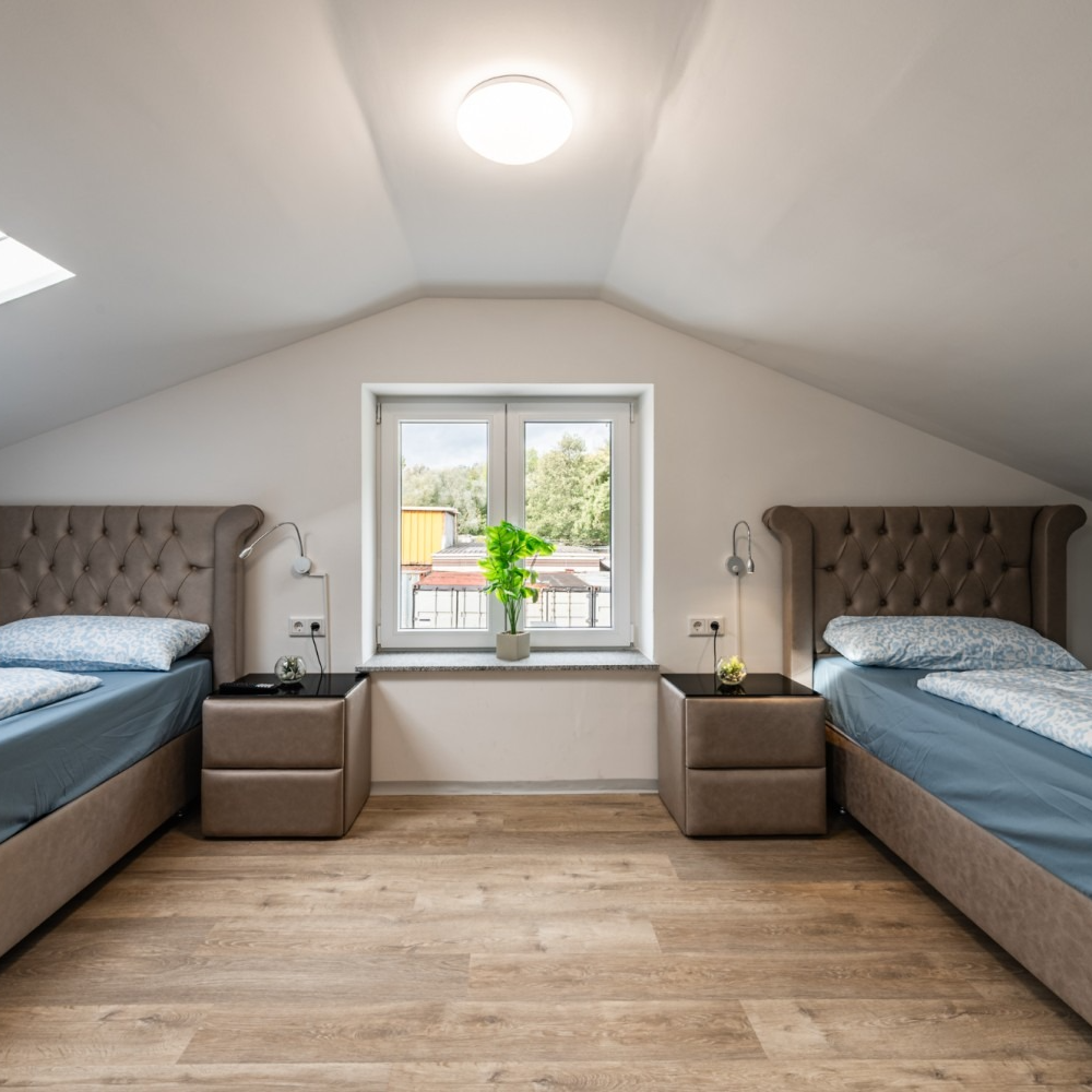 Two beds in a room with a window, two nightstands, and a plant on the windowsill.