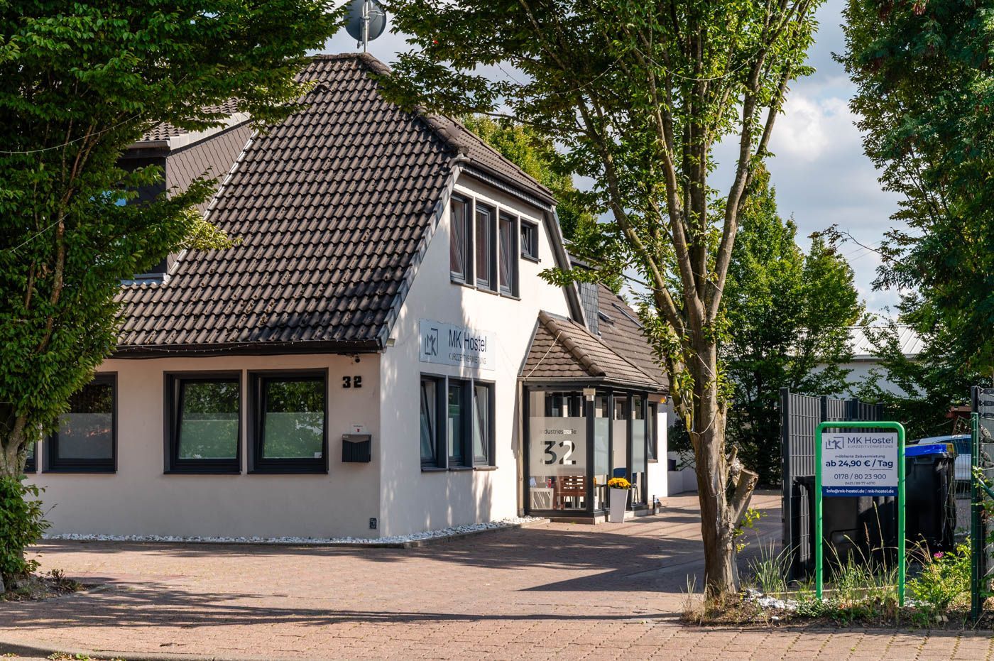 White building with a dark tiled roof, windows, and trees, with a sign in front.