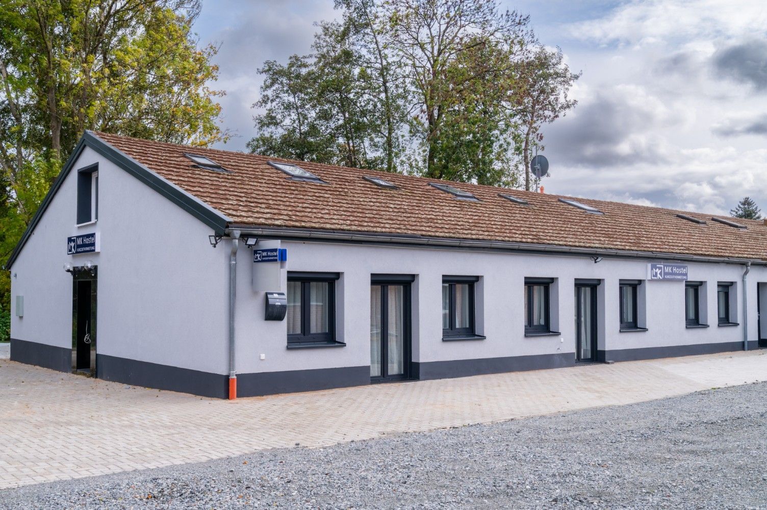 Grey and white building with brown roof and dark-framed windows under a cloudy sky.