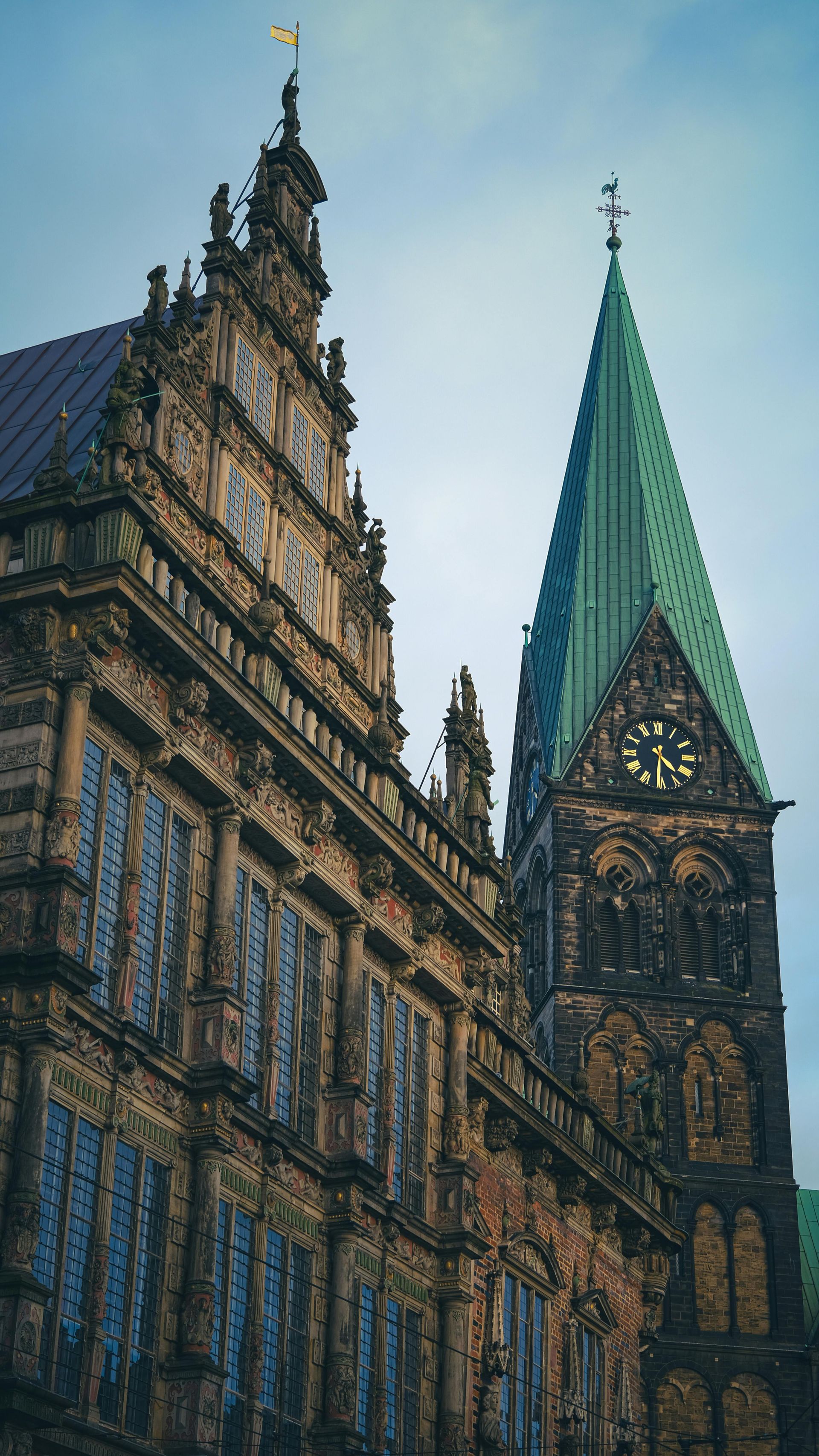 Gabled facade and green-roofed spire of Bremen City Hall, Germany, against a cloudy sky.