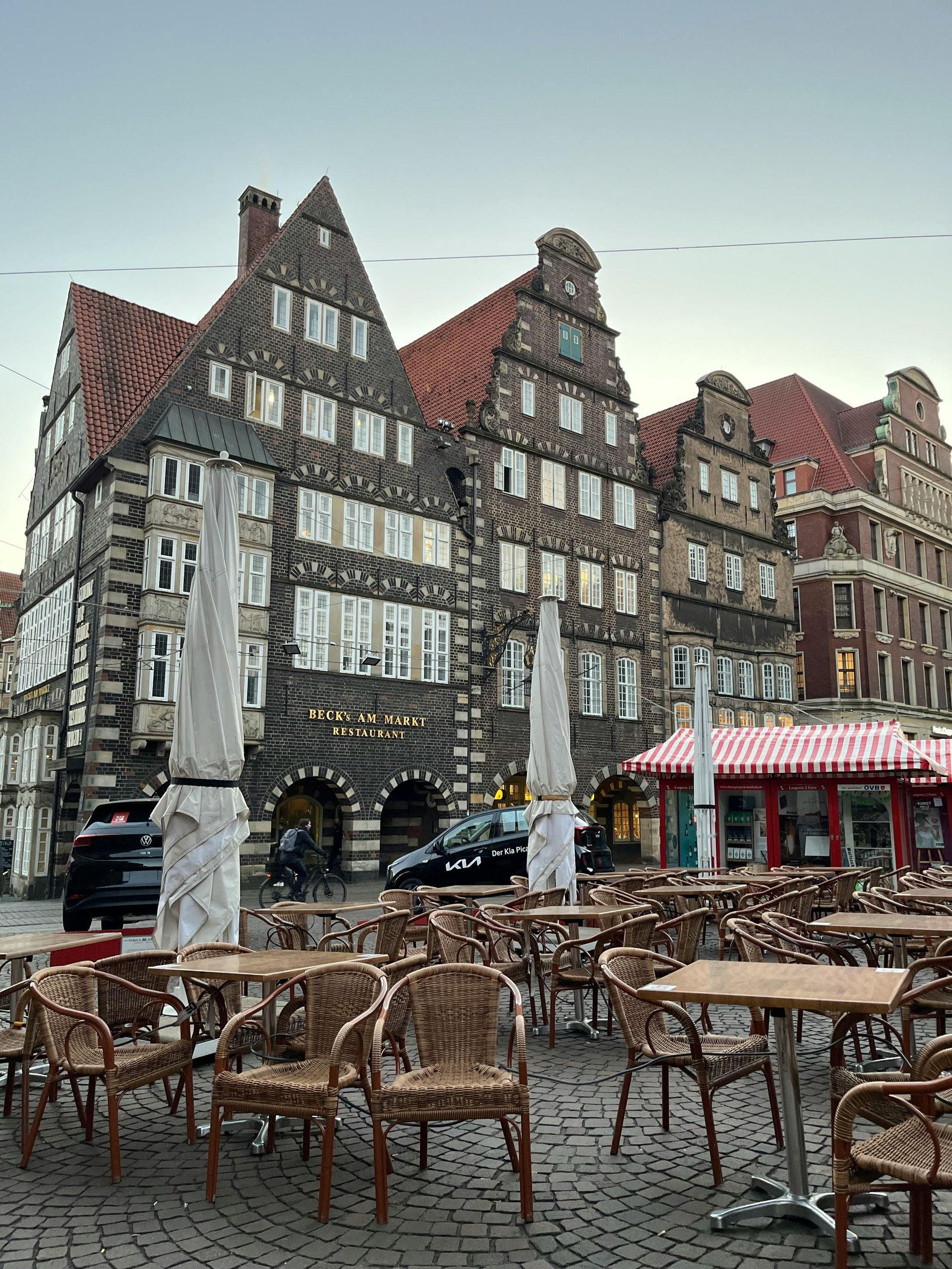 Buildings with tiered facades, red-tiled roofs, and outdoor cafe seating in a square.