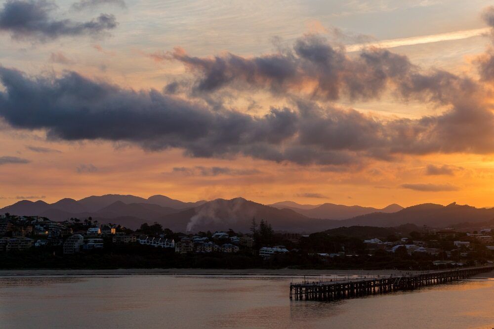 Sunset Over Water With Mountains, Clouds, and a Pier — Premier Removals & Storage In Coffs Harbour, NSW