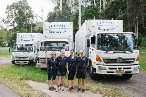 Four People in Front of Three White Moving Trucks — Premier Removals & Storage In Boambee, NSW