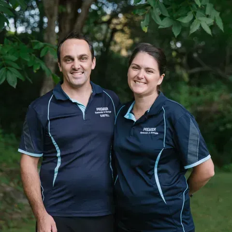 Two Smiling People in Matching Blue Polo Shirts — Premier Removals & Storage In Boambee, NSW
