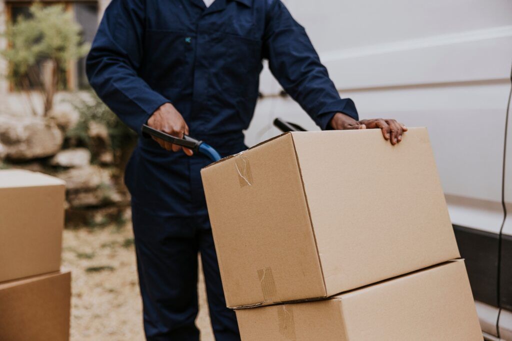A Person Carrying Two Stacked Cardboard Boxes — Premier Removals & Storage In Boambee, NSW