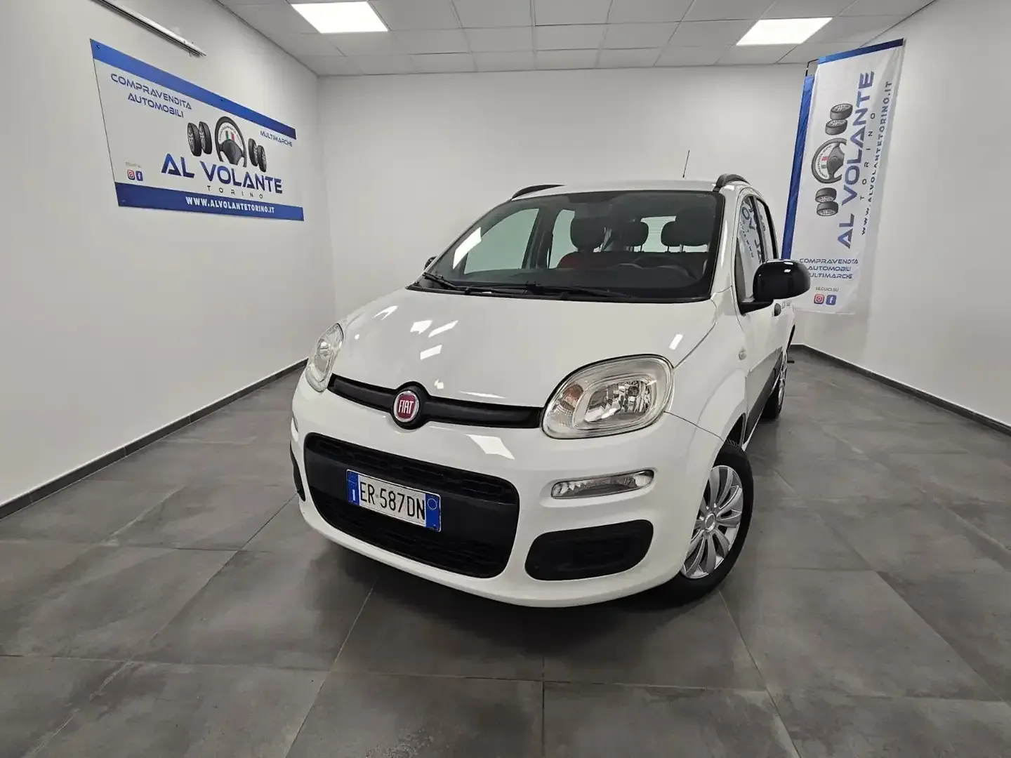 Una Fiat Panda bianca parcheggiata in uno showroom interno ben illuminato e piastrellato, con il marchio