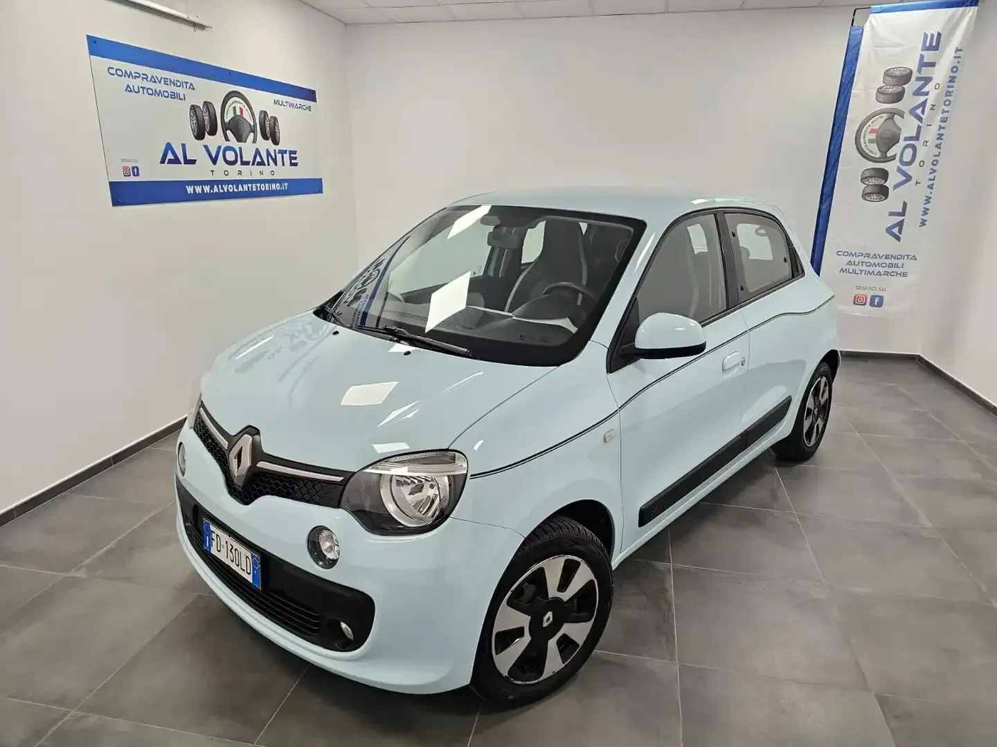 Una Renault Twingo azzurra parcheggiata in uno showroom luminoso con pareti bianche e il marchio