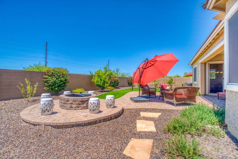 There is a fire pit in the backyard with a red umbrella.