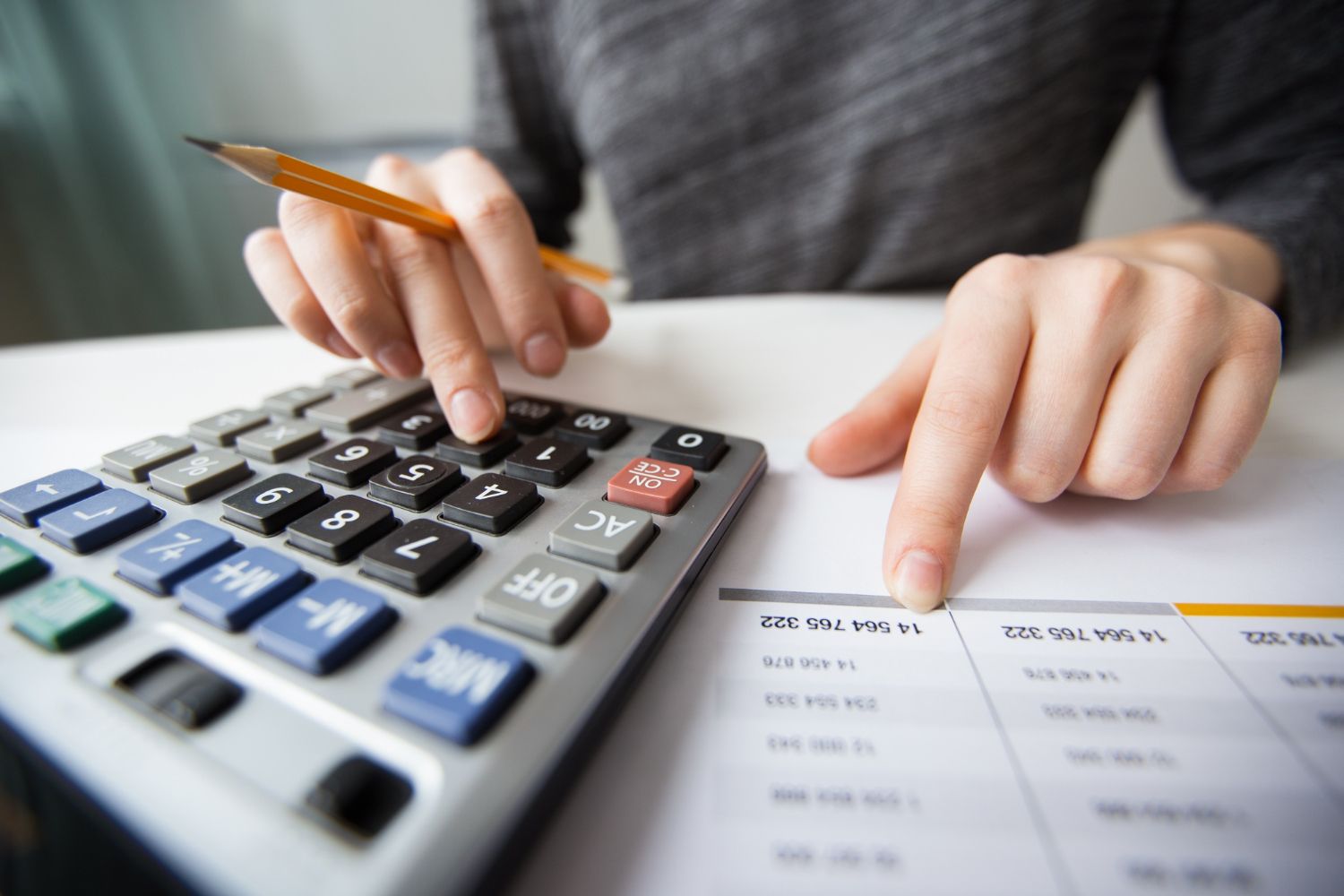 Mãos usando uma calculadora ao lado de papéis e um lápis sobre uma mesa