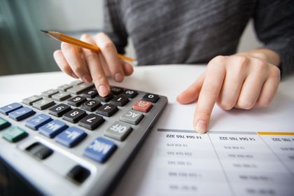 Mãos usando uma calculadora ao lado de papéis e um lápis sobre uma mesa