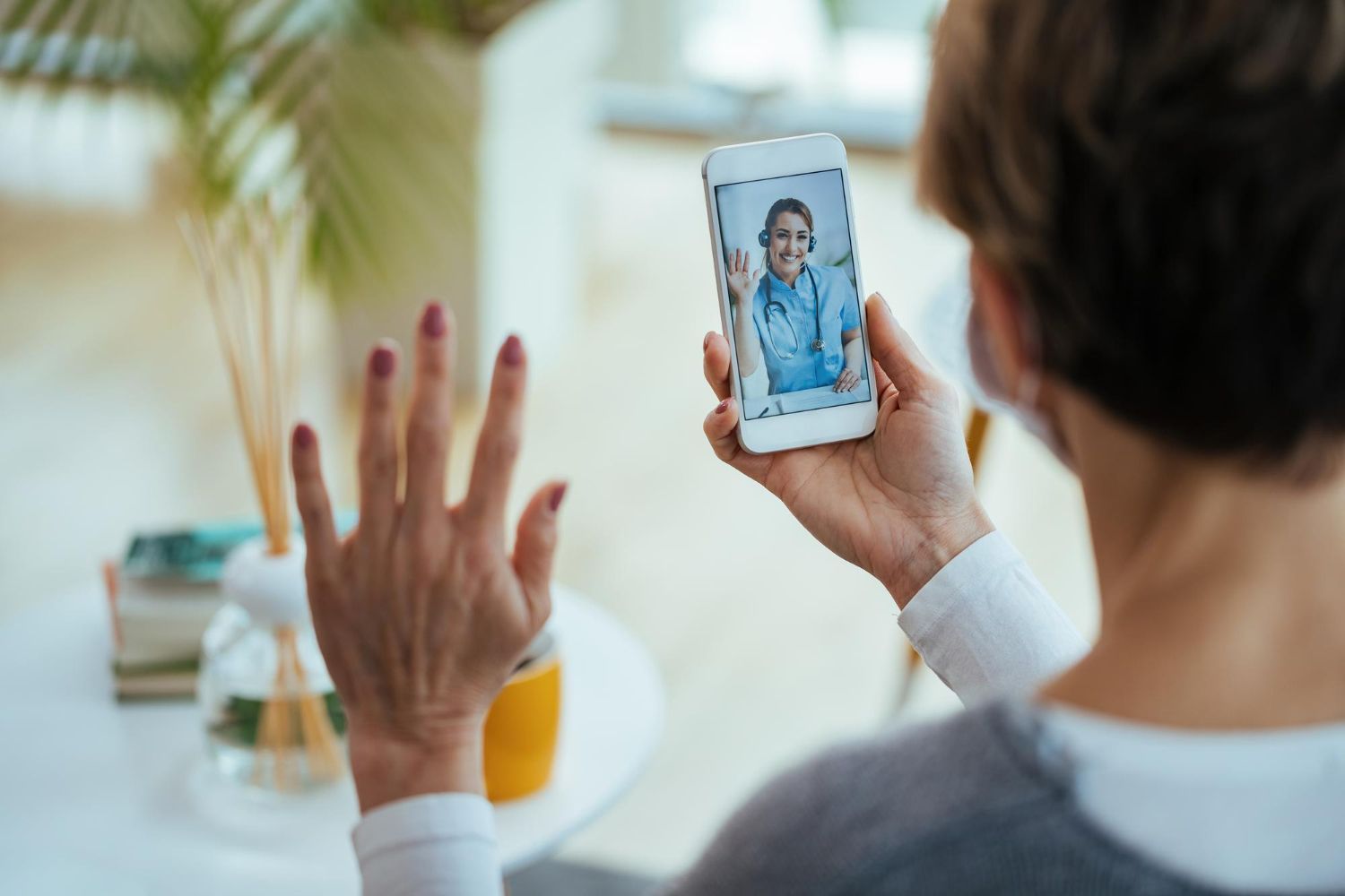 Pessoa participa de uma videochamada em um smartphone enquanto acena para a tela em um ambiente iluminado.