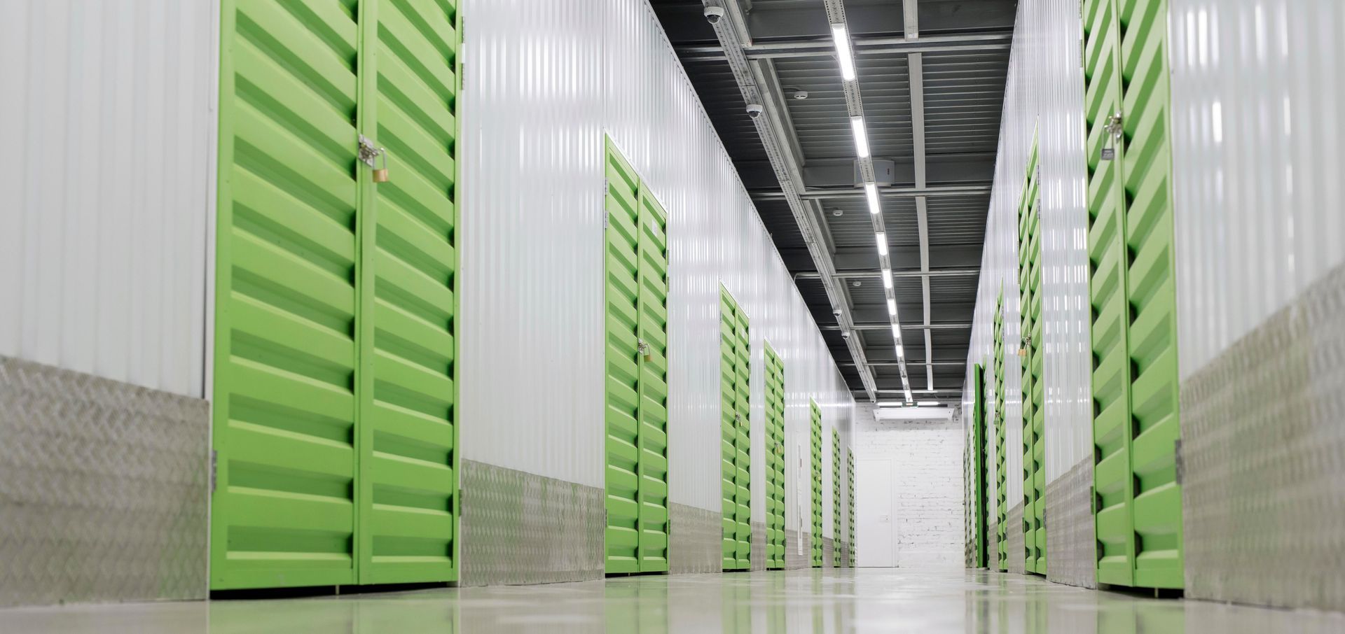 A hallway of green storage lockers in a white and silver building, perspective shot.