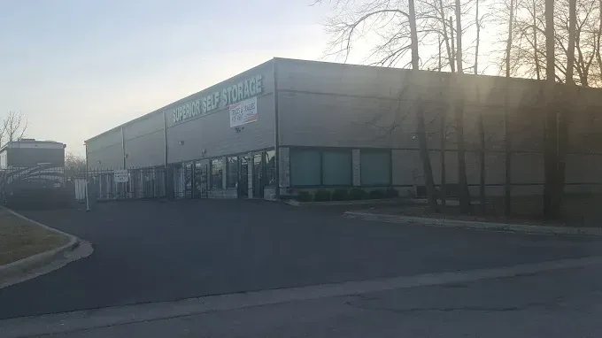 Gray commercial building with glass front, sign, and cars parked nearby.