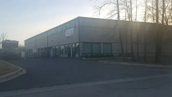 Gray commercial building with glass front, sign, and cars parked nearby.