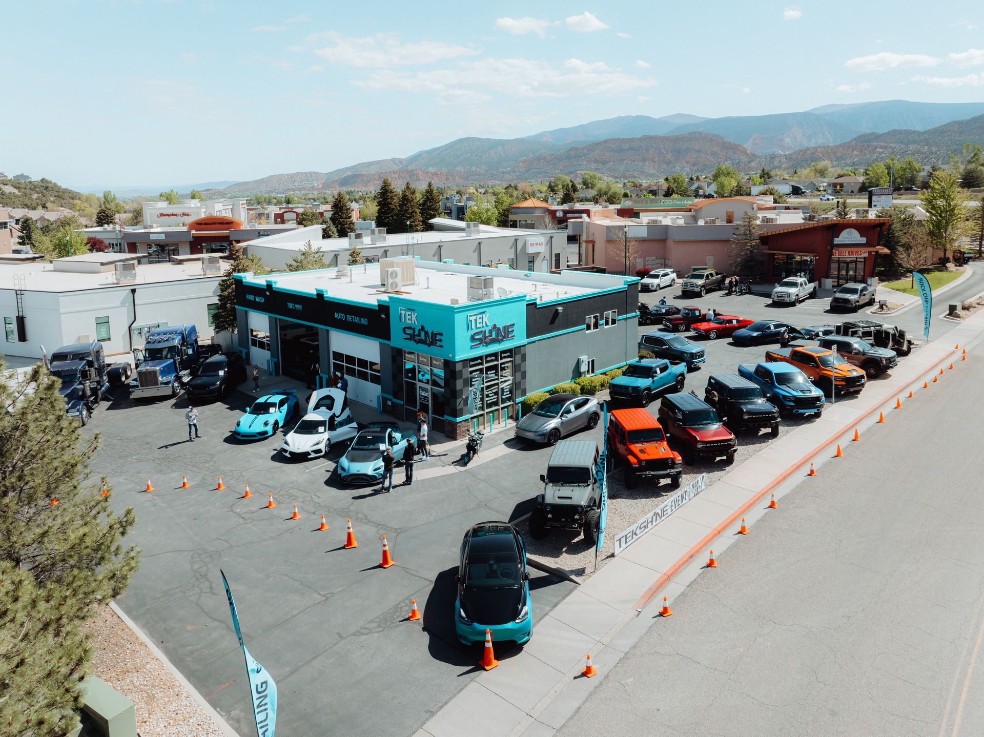 Car dealership with vehicles parked outside; mountains and town in background.