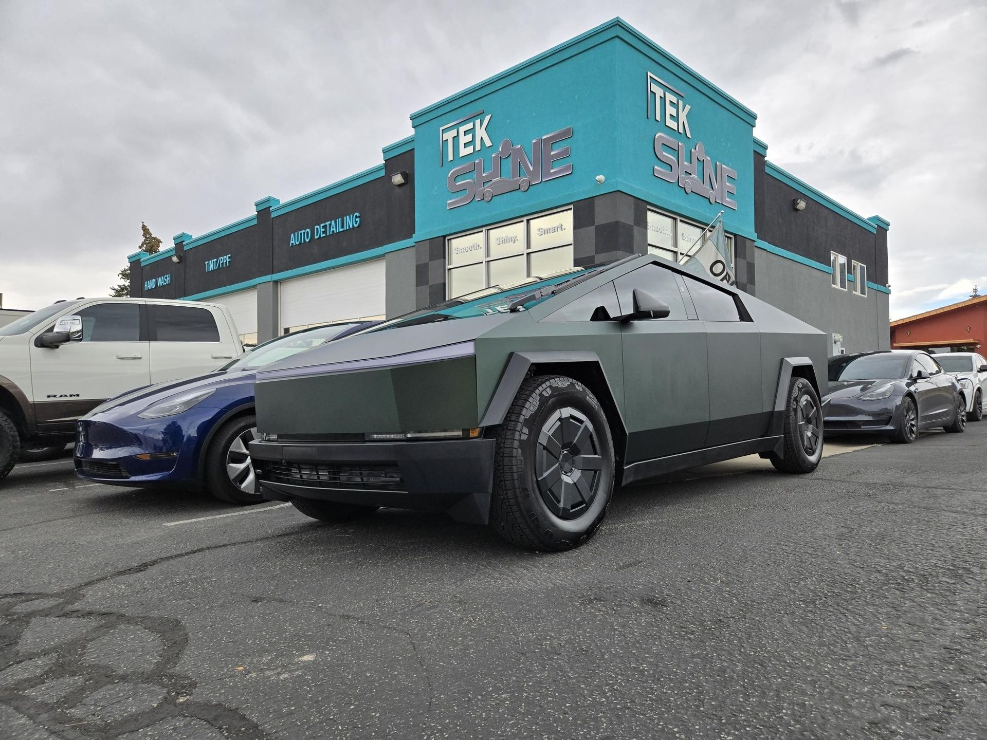 Green-wrapped Tesla Cybertruck parked in front of a Tek Shine auto shop