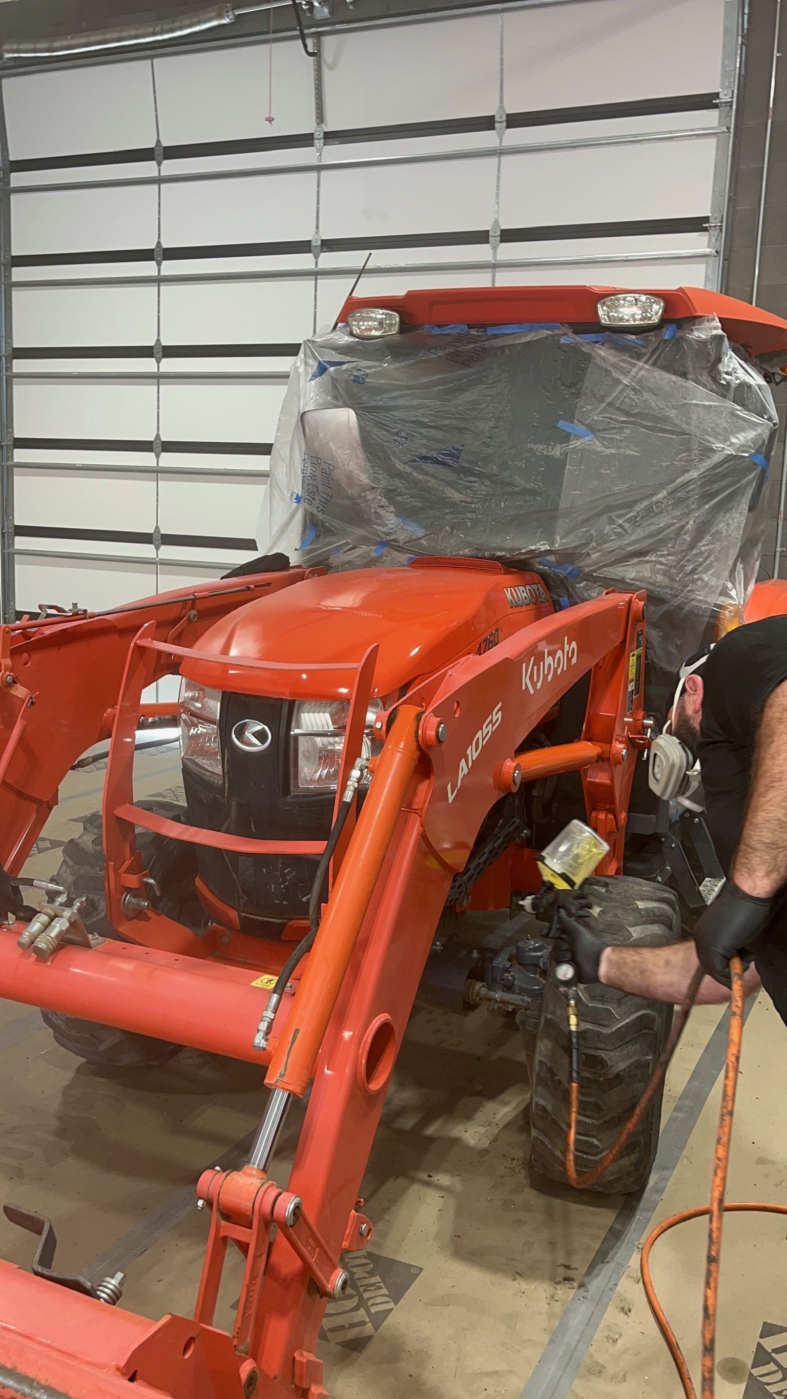 Orange tractor being washed inside a garage by a person in black gloves.