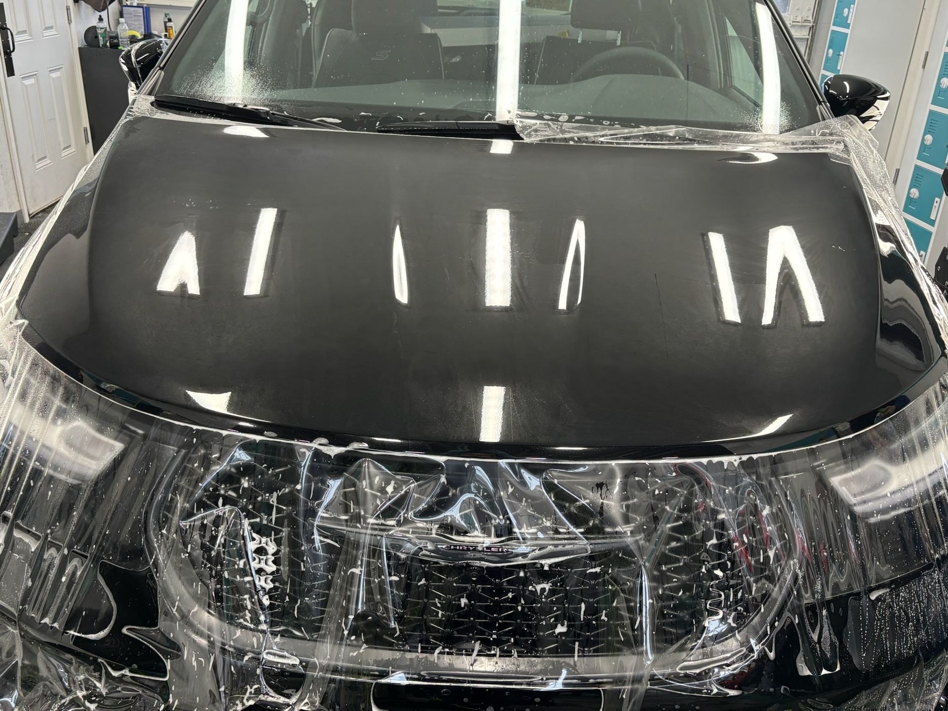 Black car hood covered in protective film, indoors.