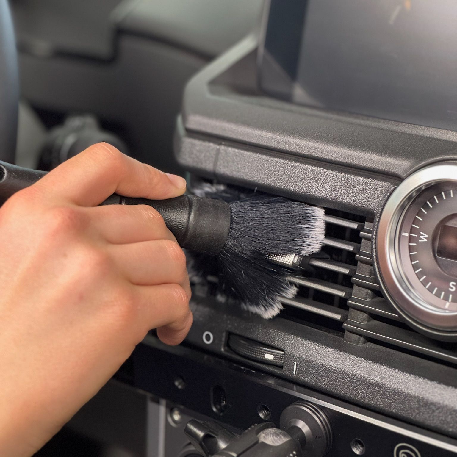 A person is cleaning the air vents of a car with a brush.