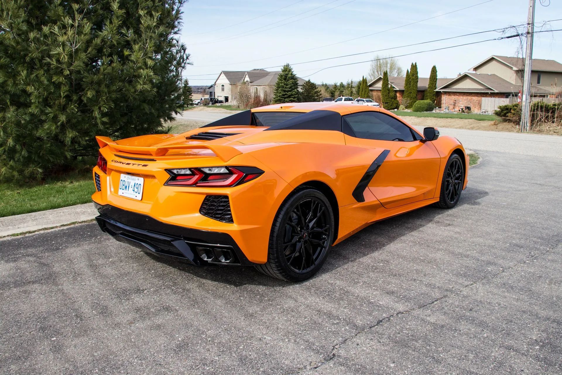 Orange Chevrolet Corvette sports car parked on a paved road near houses and trees.