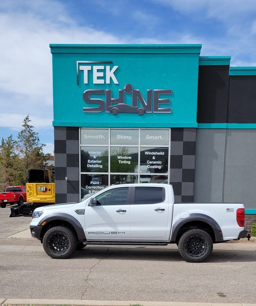 White pickup truck parked in front of a teal Tek Shine building, sunny day.