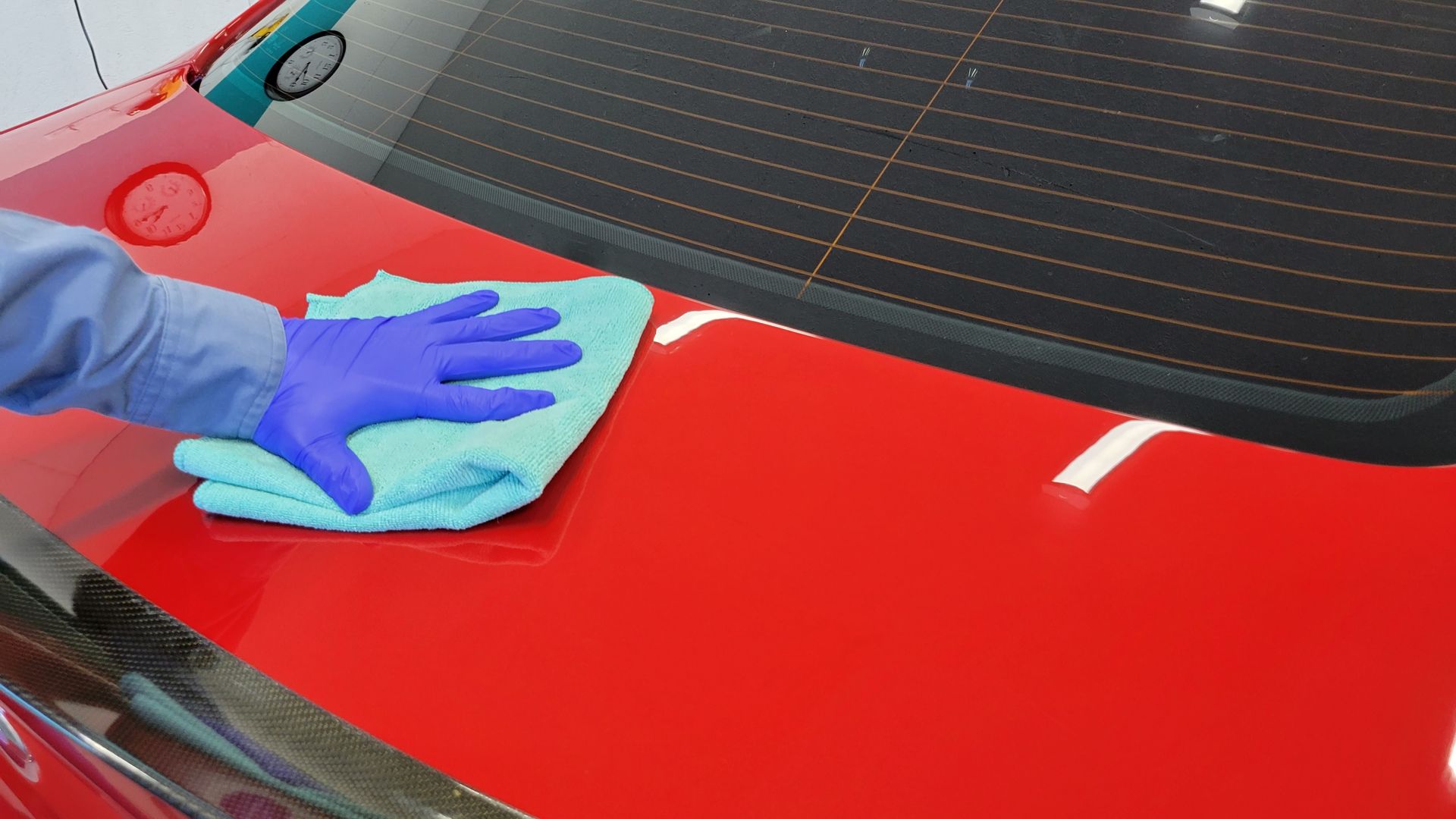 Person in blue gloves wiping red car with a blue cloth.