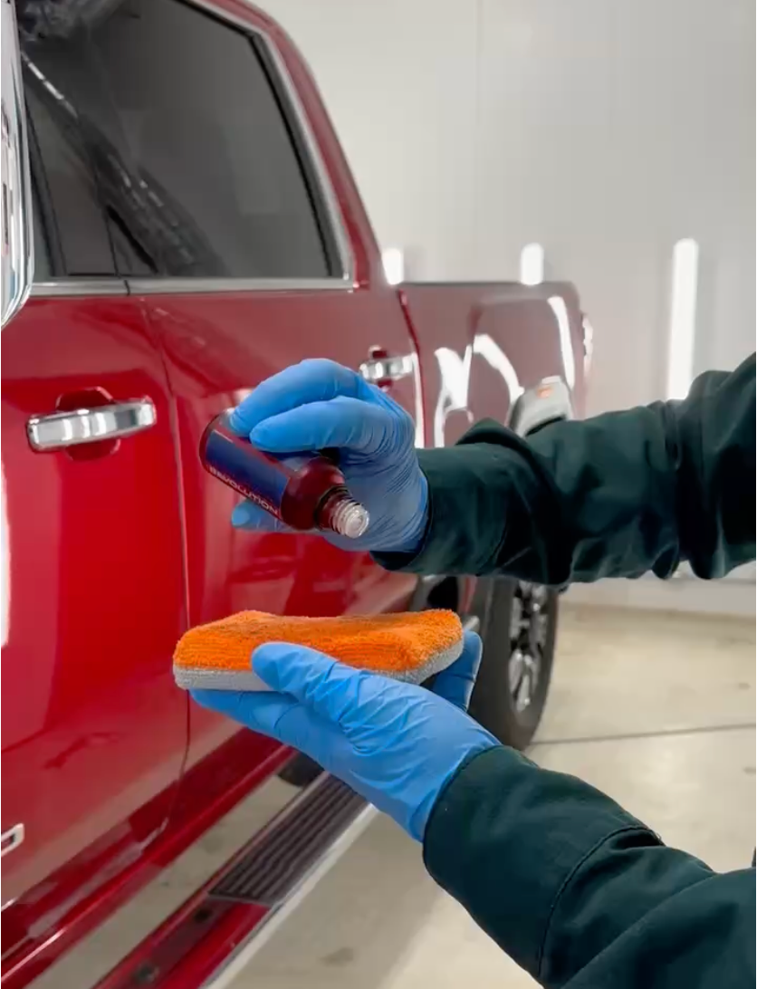A person wearing blue gloves is ceramic coating a red car