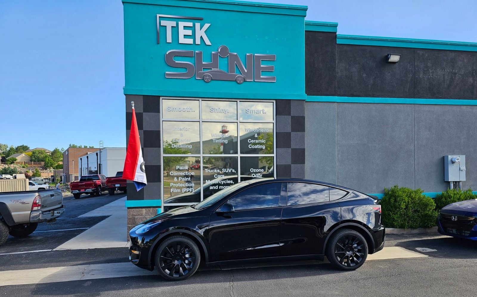 Black Tesla Model Y parked on a snowy, cracked surface, in front of a gray metal wall.