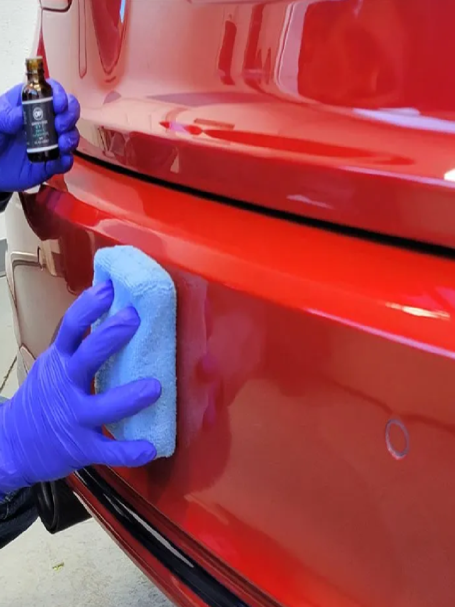 Applying ceramic coating to a red car bumper with a towel.