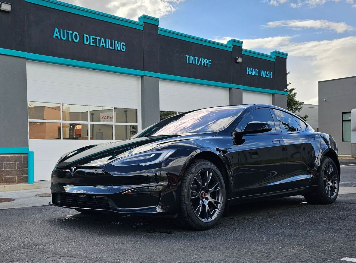 Black Tesla parked in front of Tek Shine auto shop with teal sign.