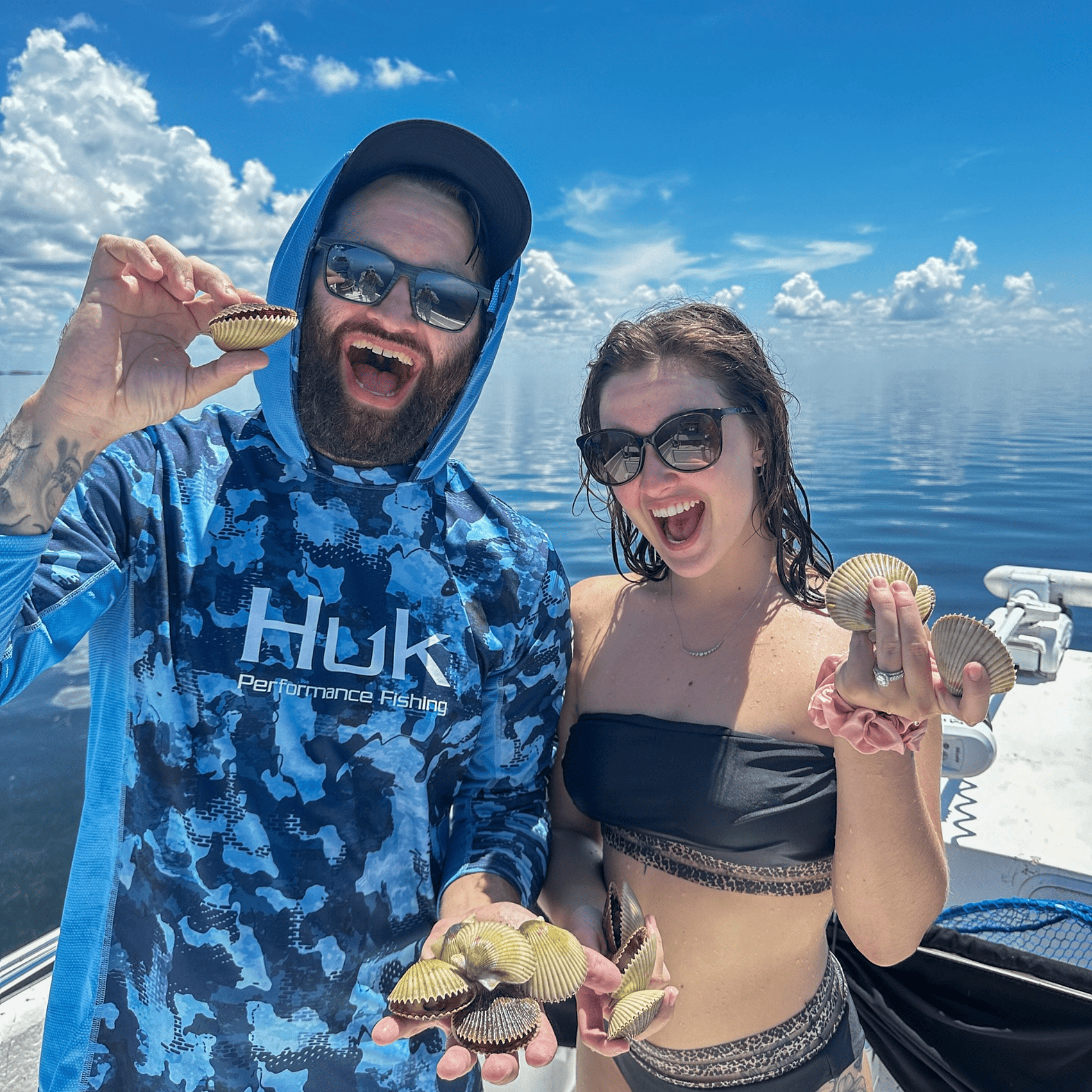 A man and a woman are standing on a boat holding oysters.