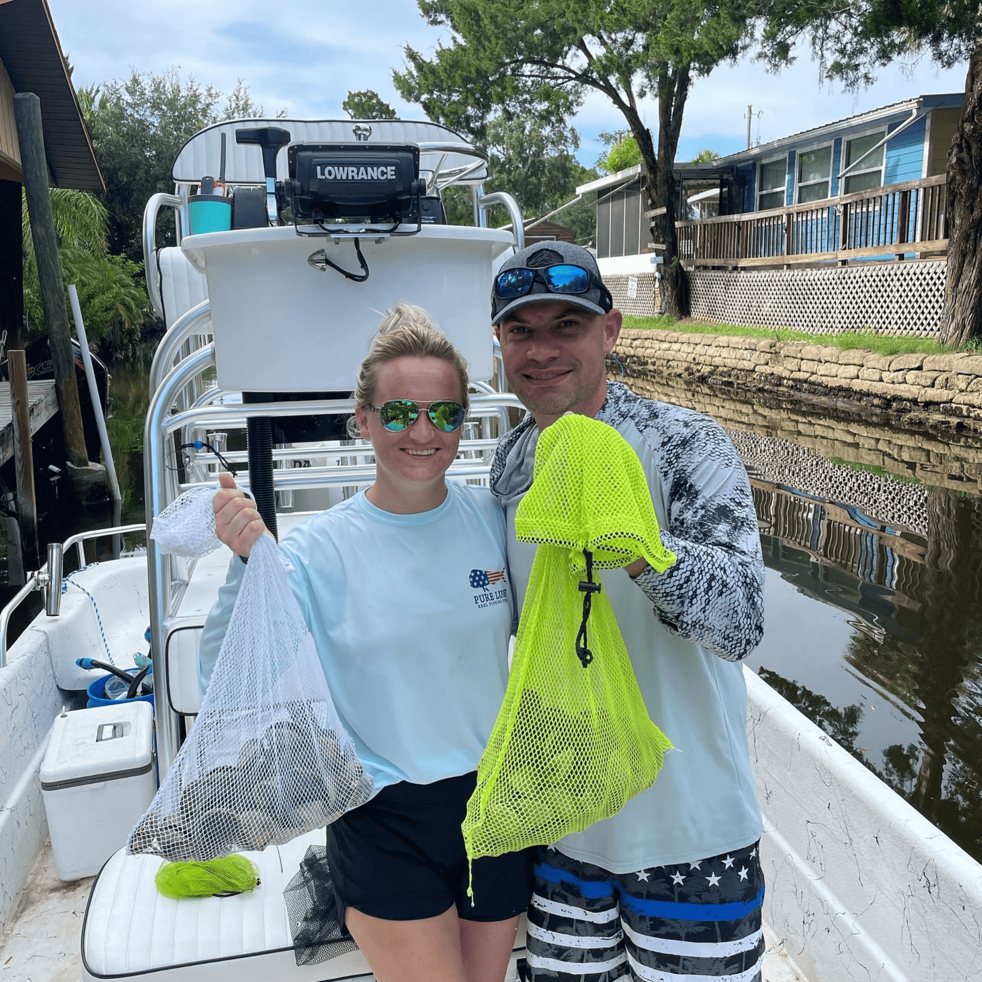 A man and a woman are standing on a boat holding bags of scallops.