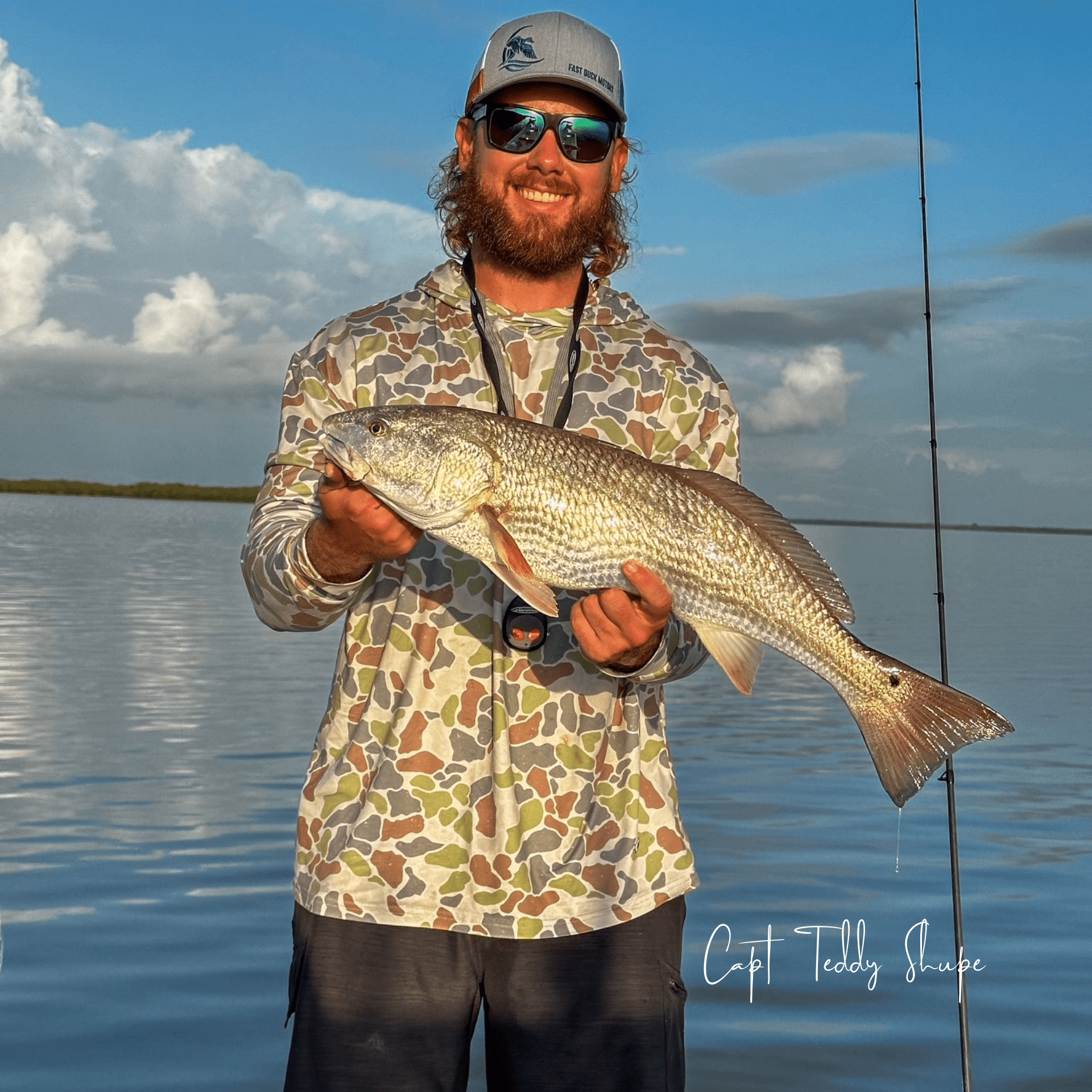 Captain Teddy Shupe wearing sunglasses and a hat is holding a large fish in his hands.