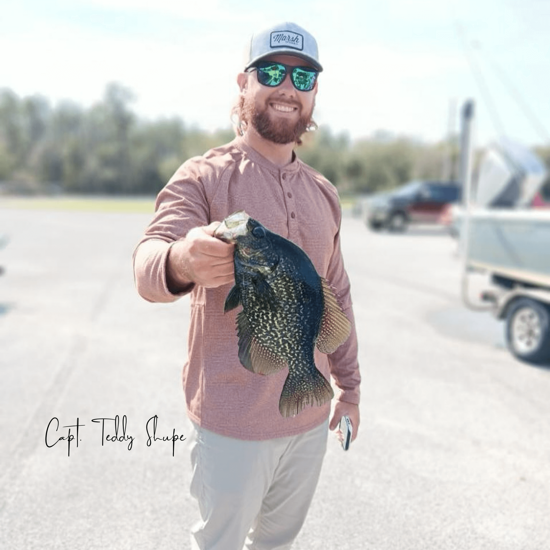 A man wearing sunglasses and a hat is holding a fish