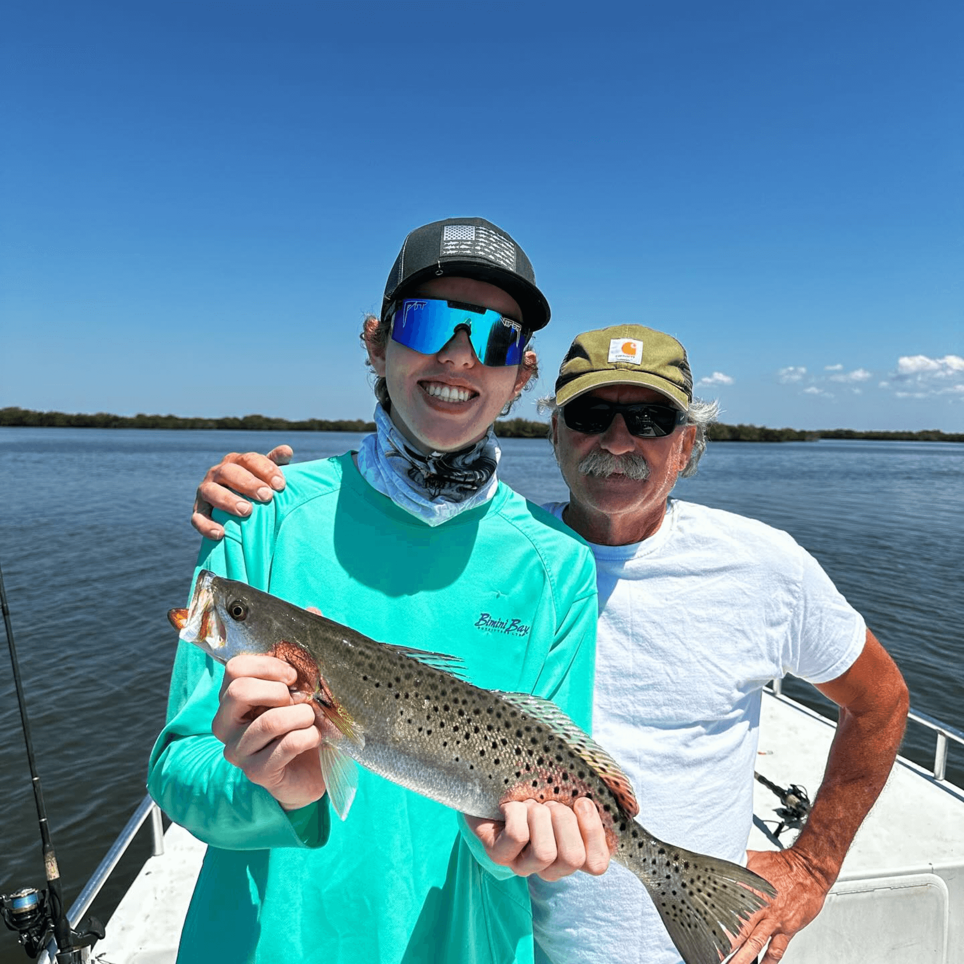 A man and a boy are standing on a boat holding a fish.