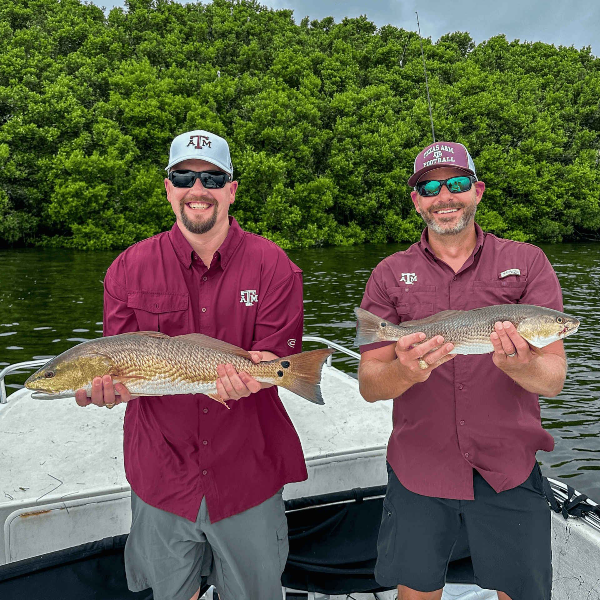 Two men are standing on a boat holding fish in their hands.