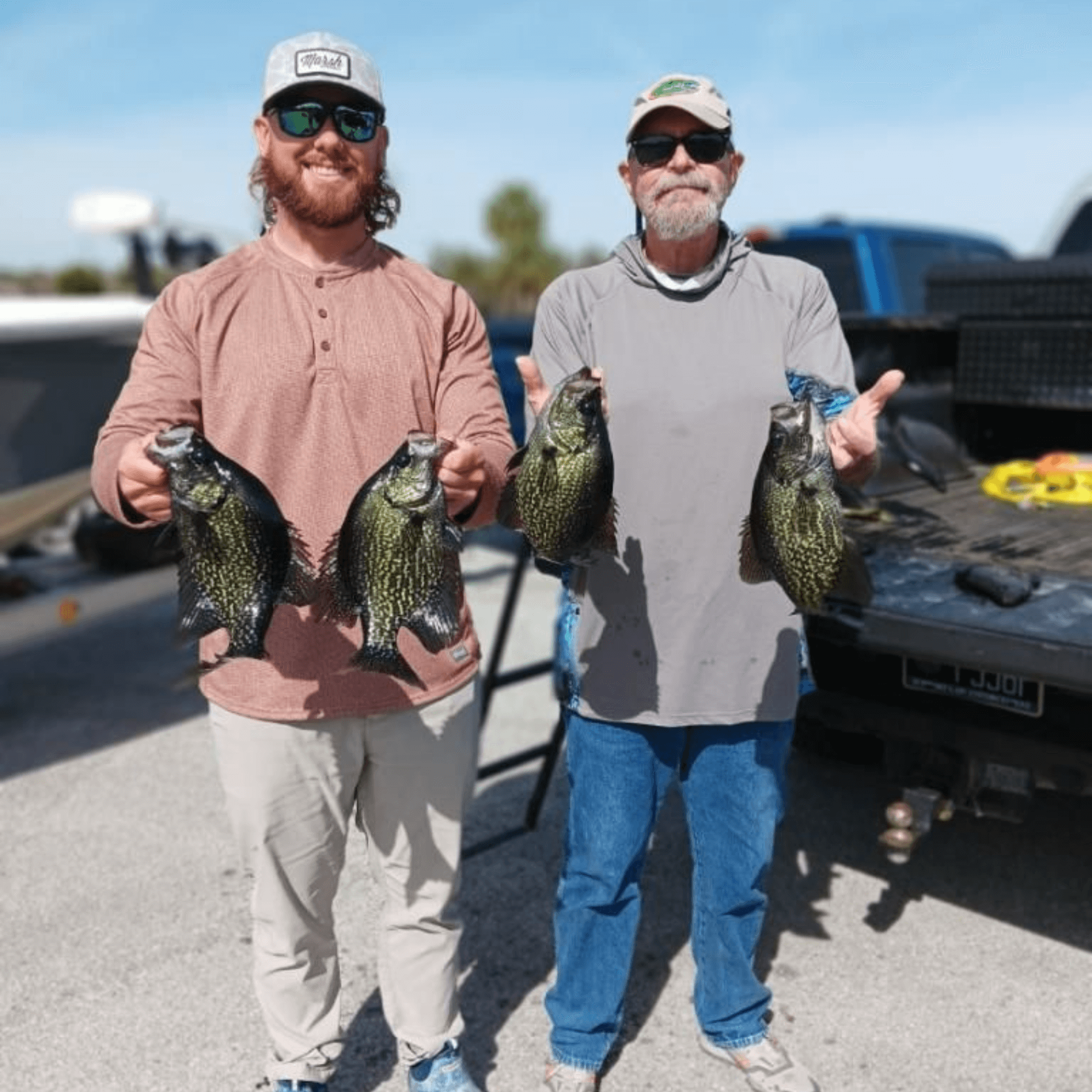 Two men are standing next to each other holding fish in front of a truck.