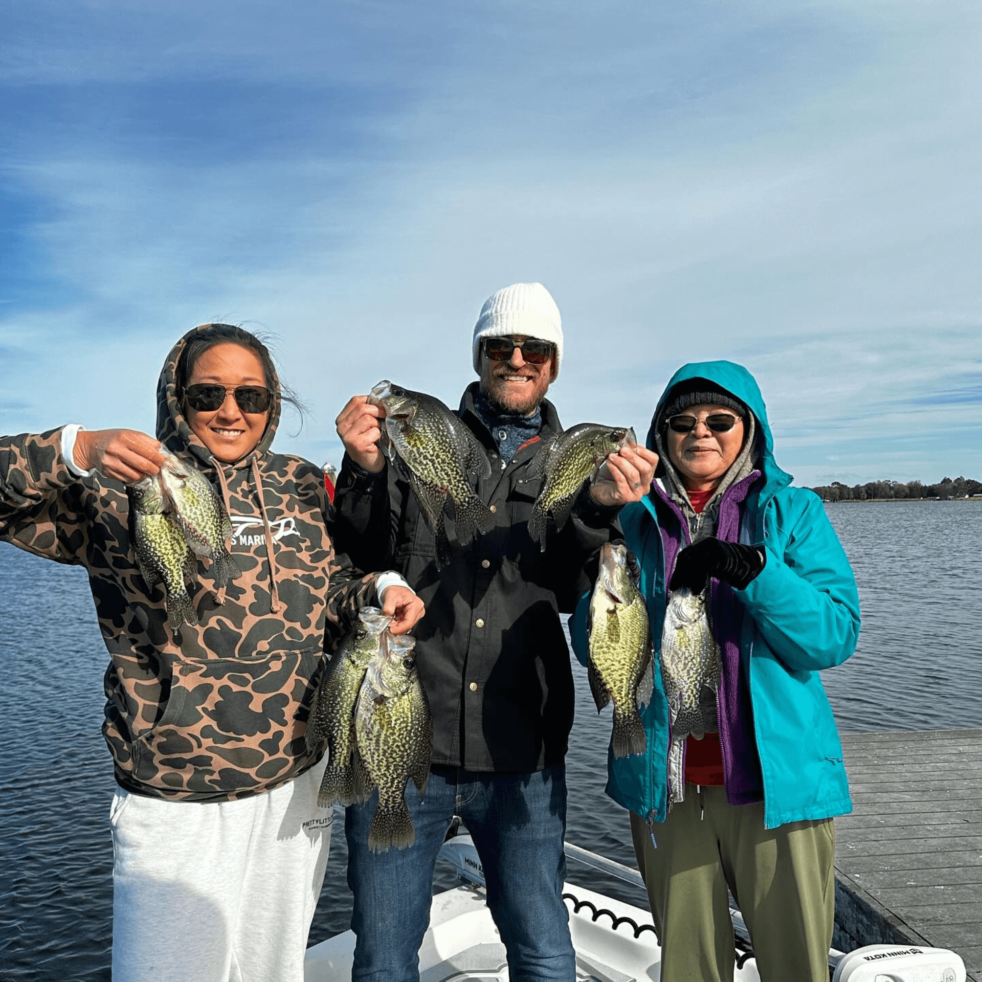 Three people are standing on a boat holding Crappie in their hands.