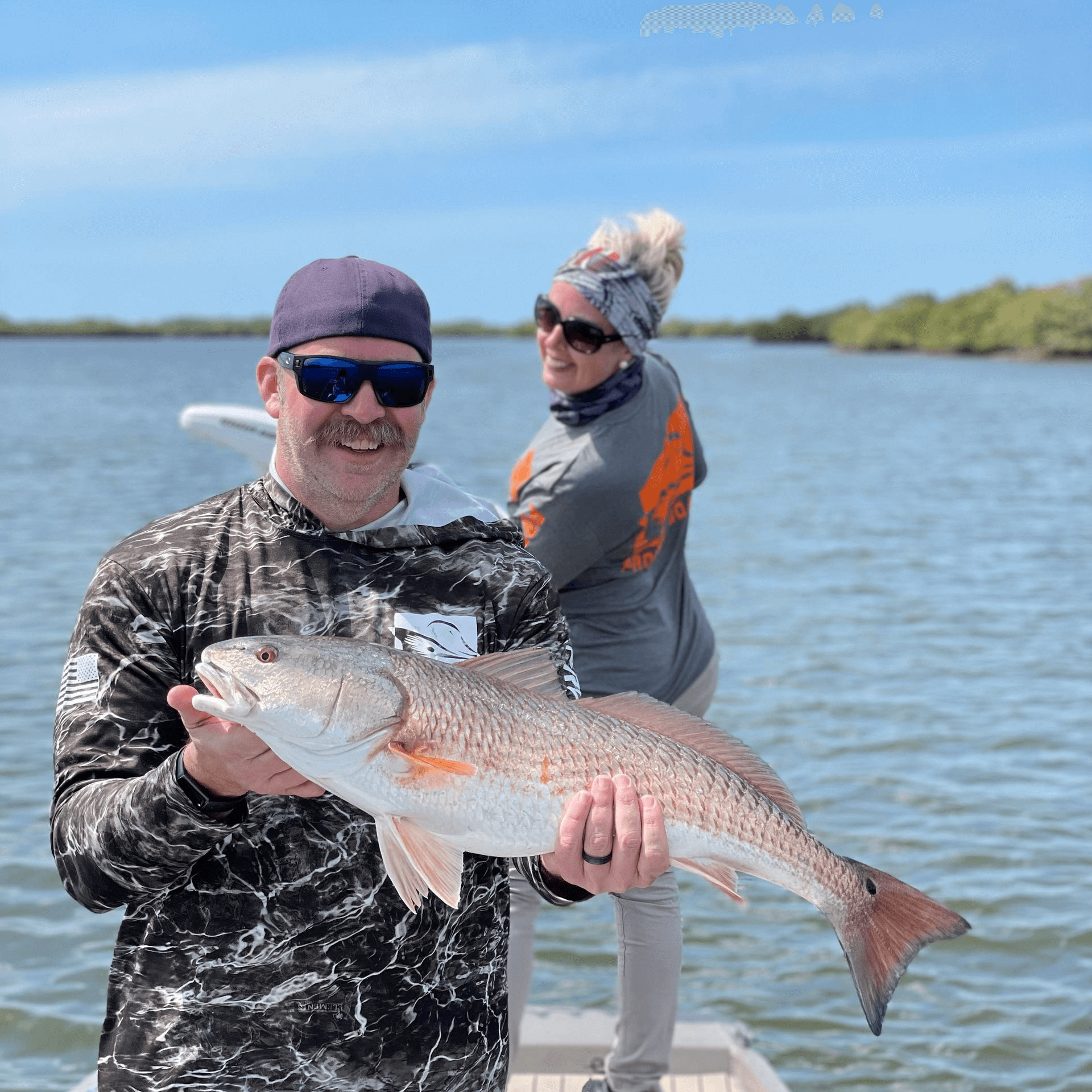 A man and a woman are standing on a boat holding a large Redfish.