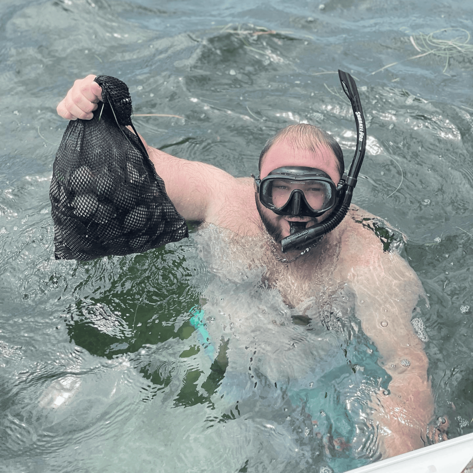 A man wearing a mask and goggles is holding a bag in the water