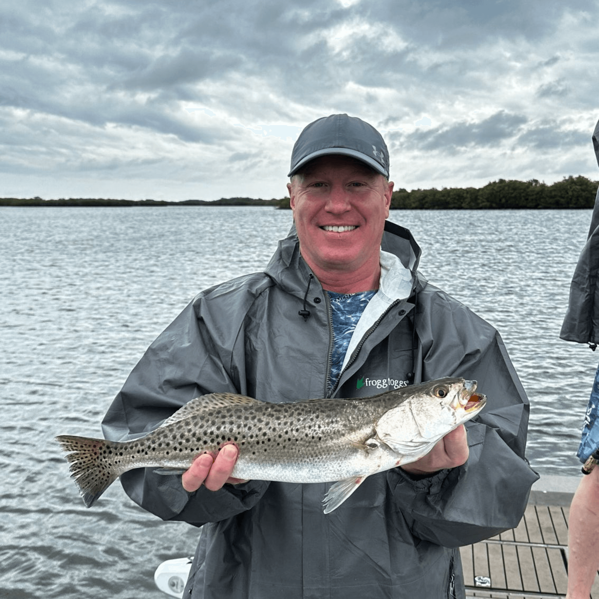 A man is holding a Speckeld Trout in his hands in front of a body of water.