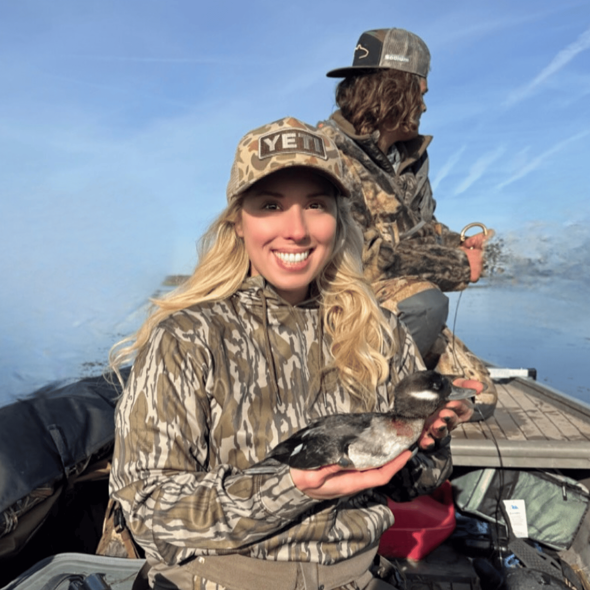 A woman is holding a duck in her hand while sitting in a boat.